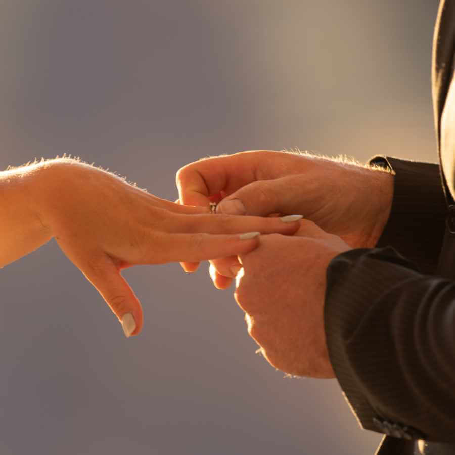 A close-up photo of a groom placing the wedding ring on his bride's finger.