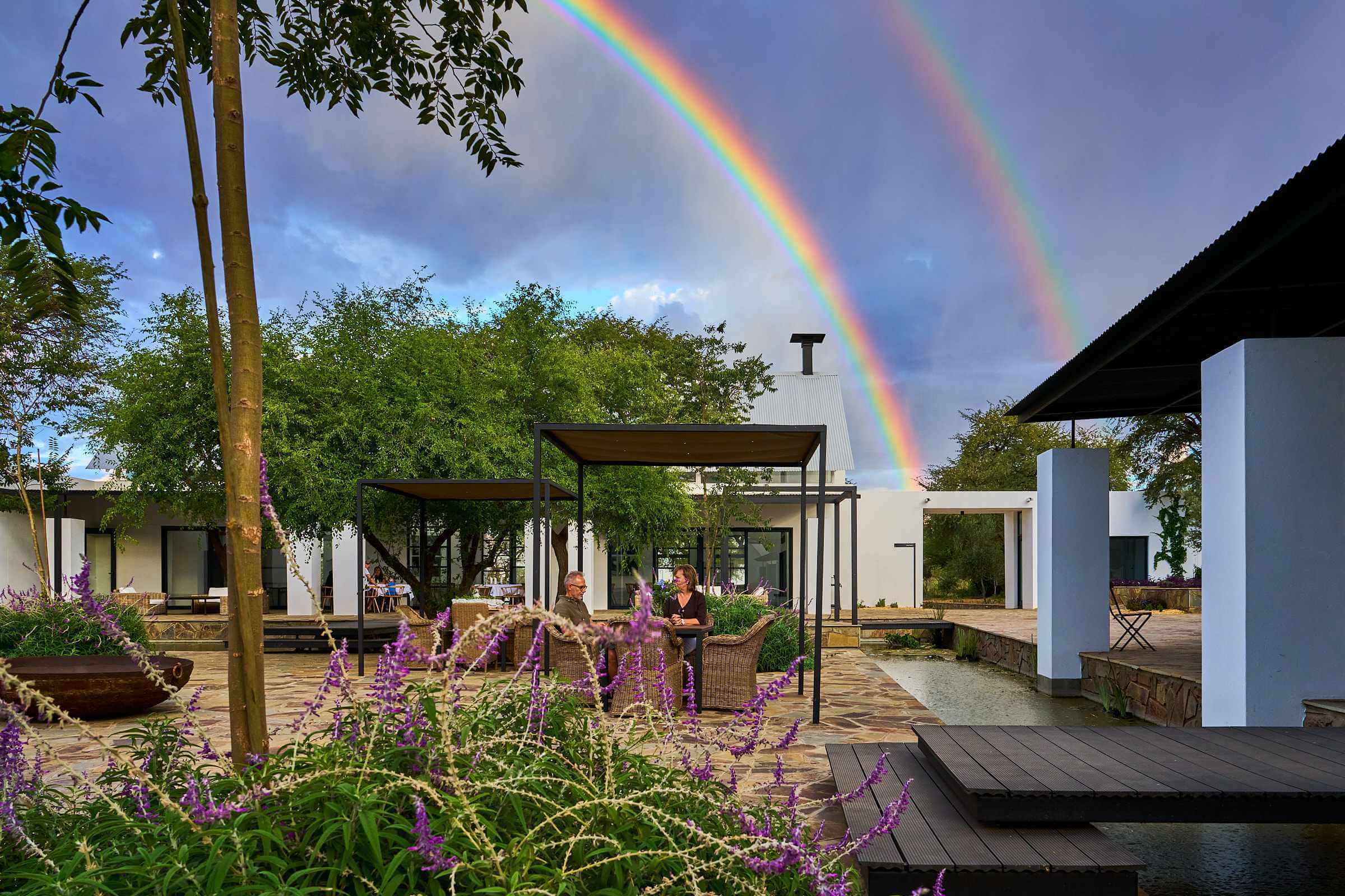 A couple enjoying a glass of wine in the tranquillity of the outside of the Sandwerf restaurant with a rainbow spanning the skies above.